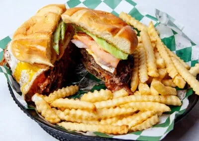 Burger cut in half with fried egg, cheese, and crinkle fries.