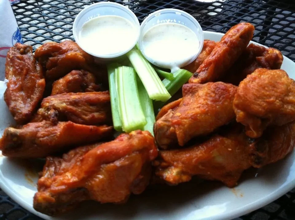 Close-up of buffalo wings, celery, and dipping sauce on an outdoor table.
