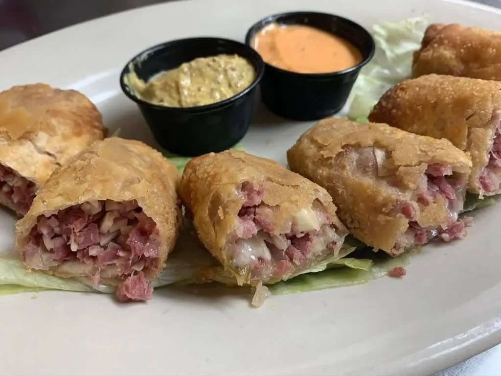 Fried rolls cut open, showing corned beef and cheese, with sauces.