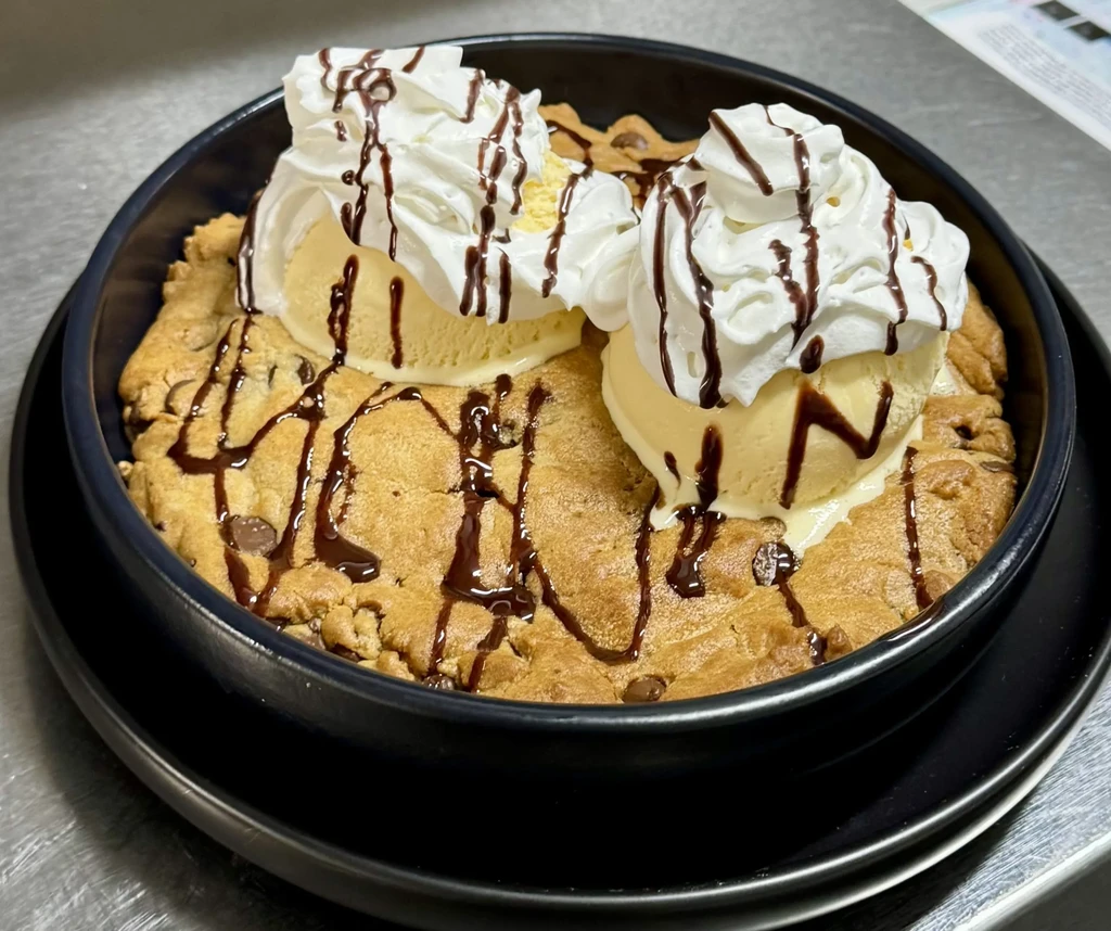 Warm chocolate chip cookie, vanilla ice cream, whipped cream, chocolate syrup in a bowl.