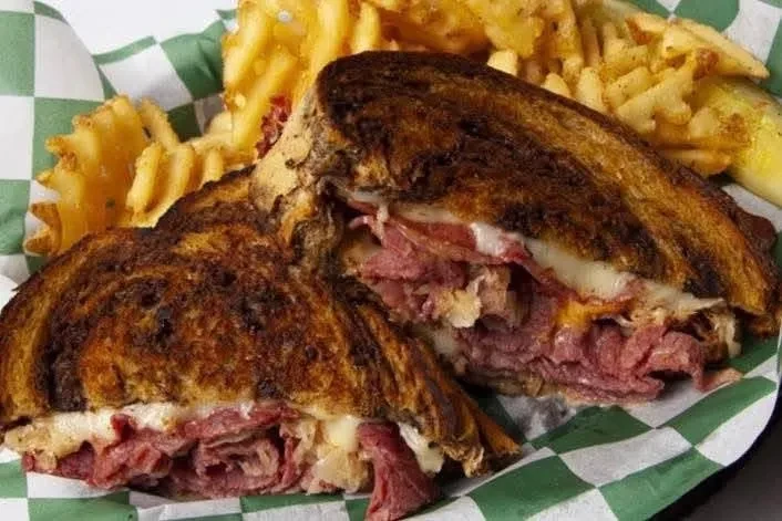 Cut grilled deli sandwich with melted cheese, waffle fries, pickle.