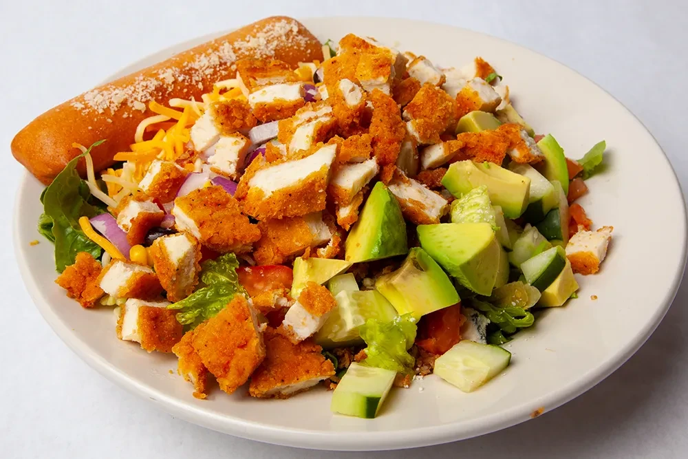 Fried chicken salad with avocado, cheese, vegetables, and a breadstick.