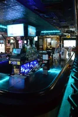 Dimly lit bar with long counter, glowing blue LEDs, and stools.