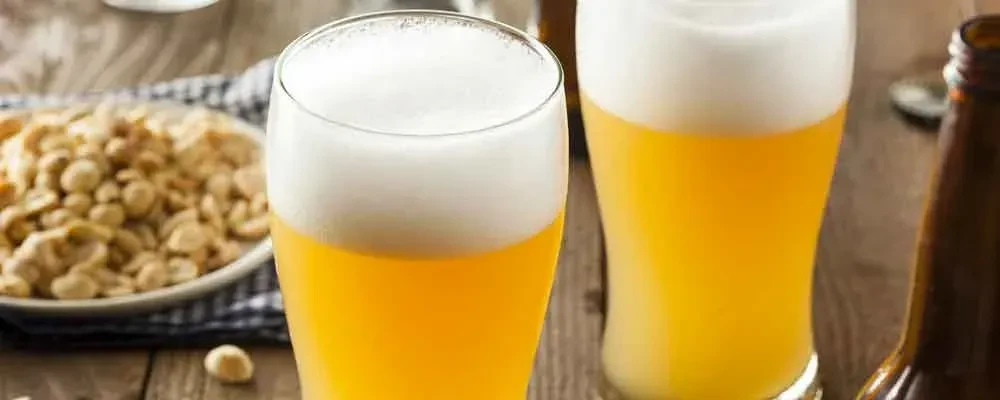 Two foamy beer glasses on a wooden table with snacks.