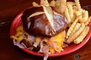 Large pretzel bun sandwich with melted cheese and crinkle-cut fries.