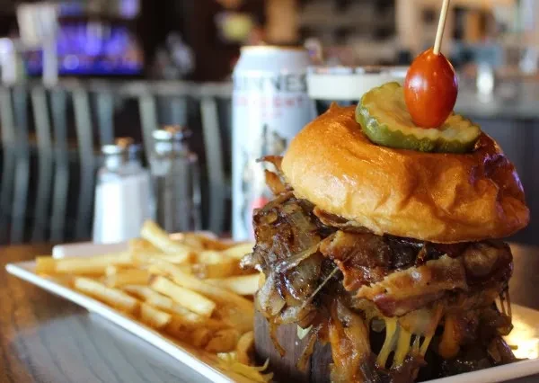 Loaded burger, golden fries, and a blurred Guinness can on a table.
