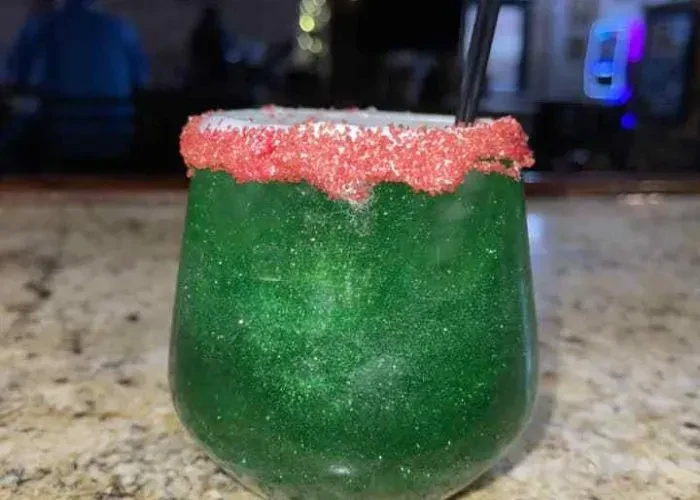 Glittery green drink with red sugar rim on a bar counter.