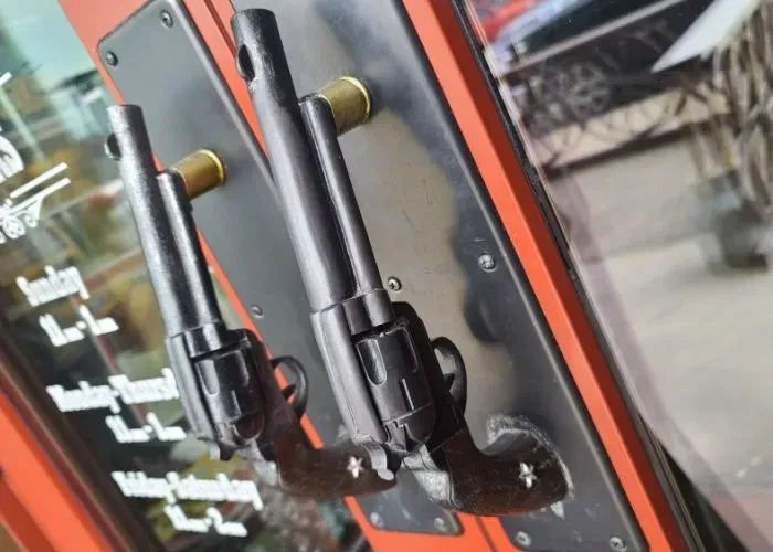 Two black revolver-shaped door handles on an orange glass door.