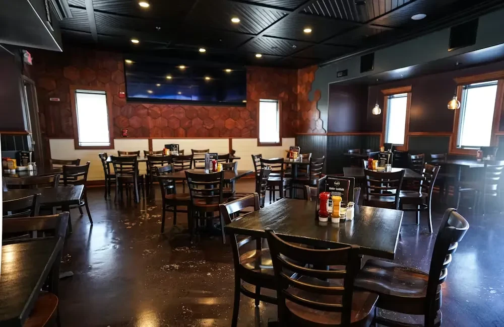 Modern restaurant dining room with dark tables and hexagonal wood wall.