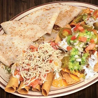 Platter with quesadillas, cheesy flautas, and loaded nachos on wood.