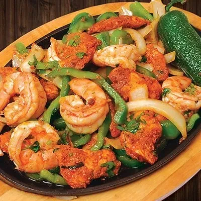 Sizzling shrimp and chicken fajitas with peppers and onions on a black skillet.