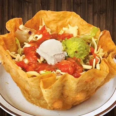 Taco salad in a crispy tortilla bowl with meat, cheese, salsa, guacamole.