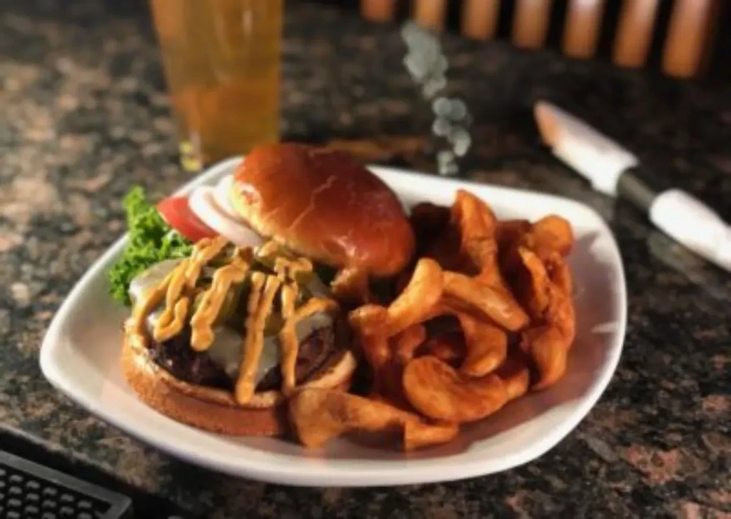 Gourmet burger with curly fries and a drink on a dark counter.