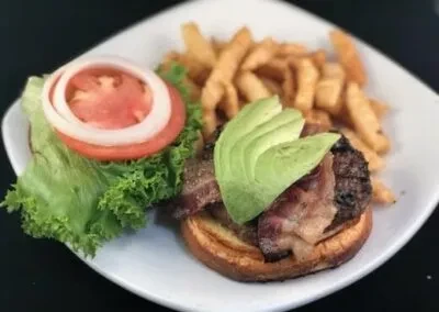 Open-faced burger with bacon, avocado, and a side of fries.