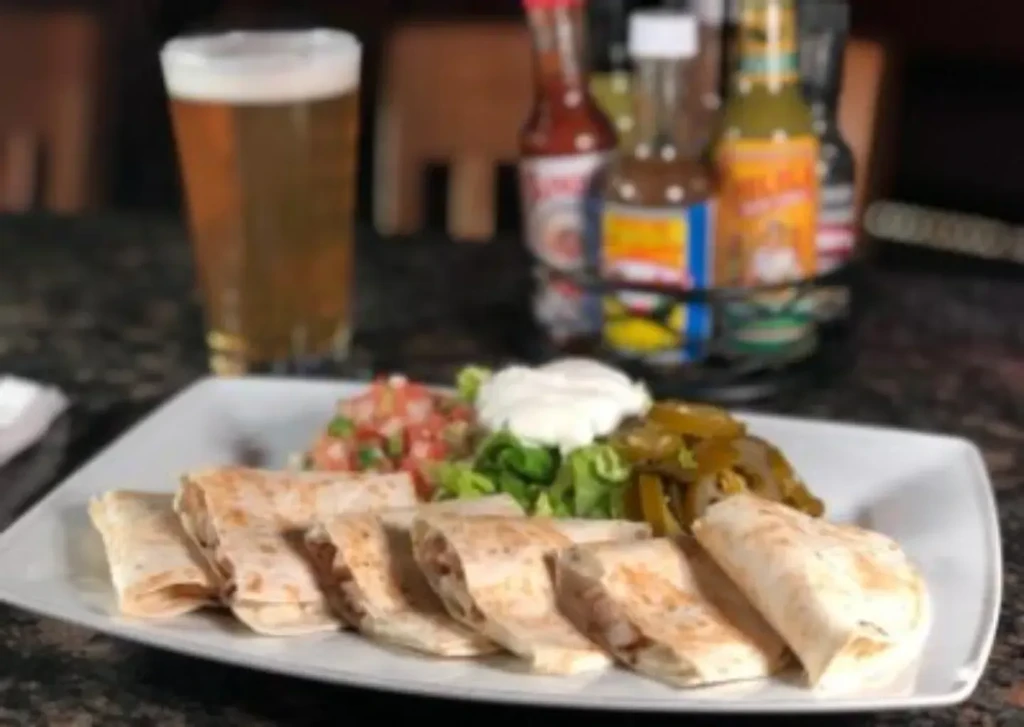 Plate of burritos or taquitos with salsa, sour cream, and jalapeños.