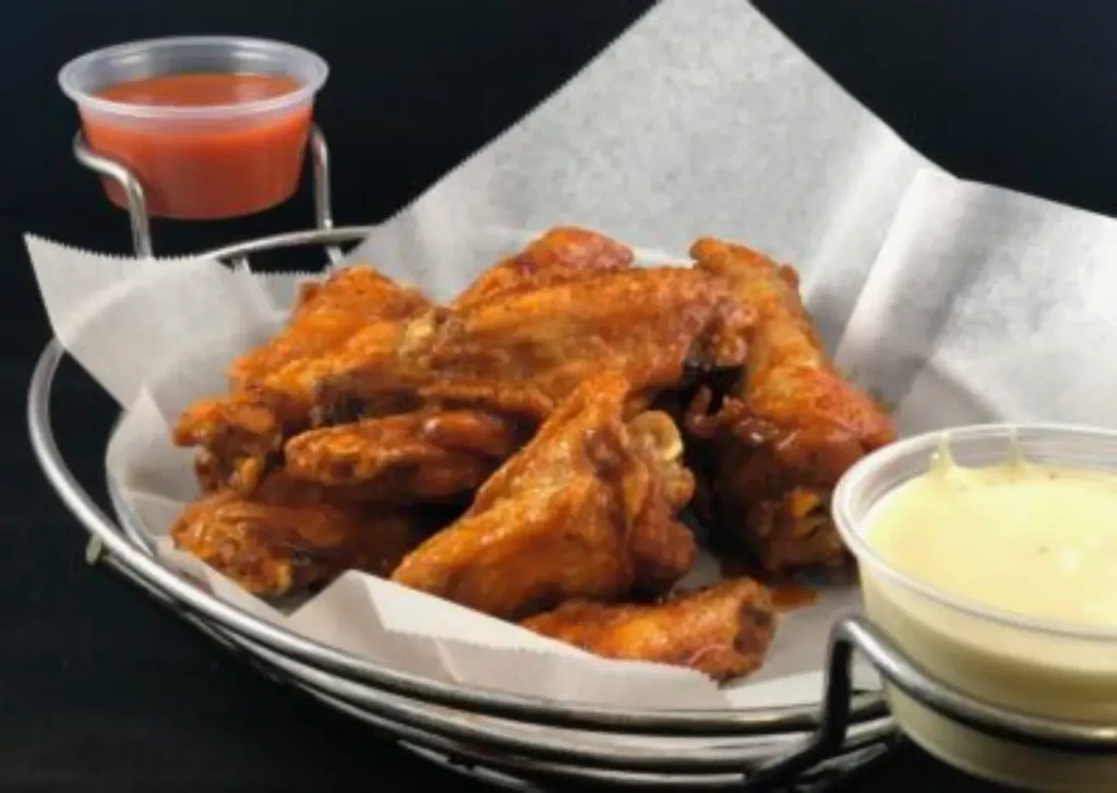 Metal basket of buffalo chicken wings with two dipping sauces.