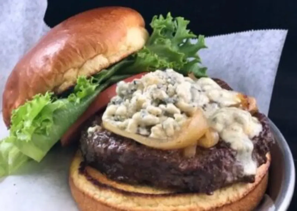 Gourmet burger with blue cheese, caramelized onions, lettuce, and tomato.