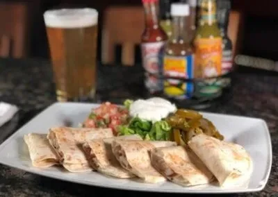 Plate of quesadilla pieces with pico de gallo, sour cream, and jalapeños.