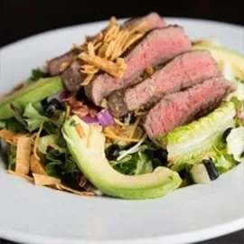 Medium-rare steak salad with avocado, black beans, and mixed greens.