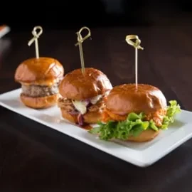 Three mini burgers with varied fillings, served on a white plate.
