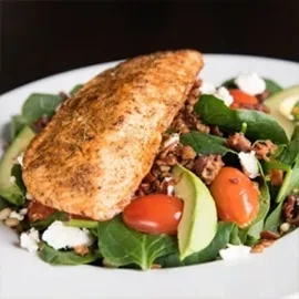 Close-up: Seasoned protein salad with spinach, tomatoes, avocado, and cheese.