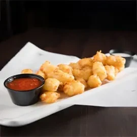Plate of golden-brown fried food with red and light dipping sauces.