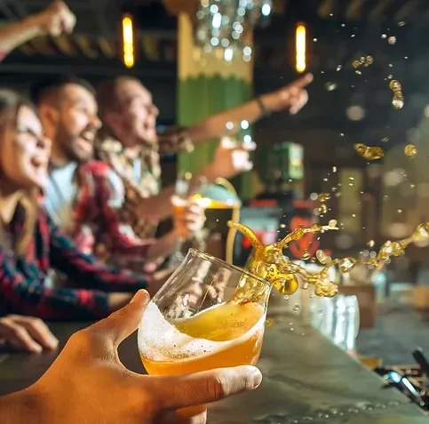 Close-up of beer splashing from a glass, blurred cheering crowd behind.