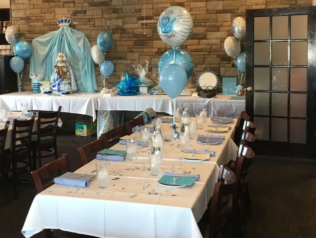 Blue and silver restaurant baby shower setup with decorated tables and diaper cake.