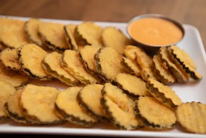 A plate of golden-brown fried pickles with orange dipping sauce.
