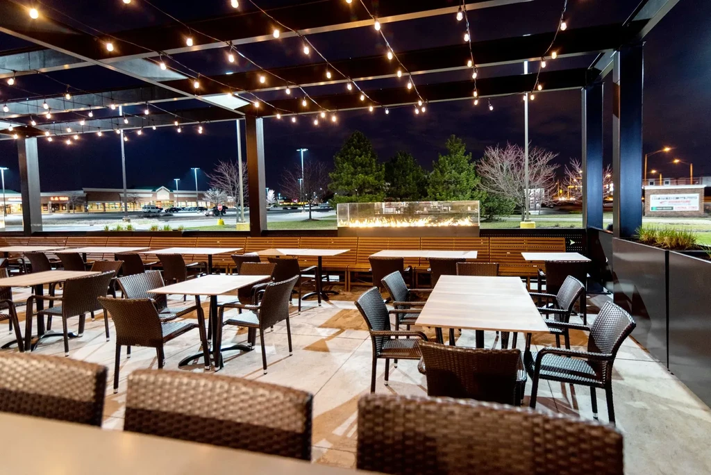 Outdoor restaurant patio at night with seating, string lights, and fire.