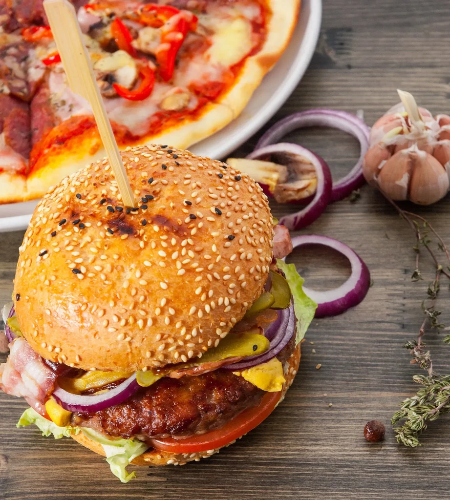 Close-up of a gourmet burger, pizza slice, garlic, and herbs.
