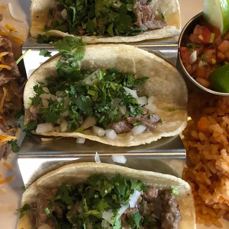 Three street tacos in a holder with pico de gallo and rice.