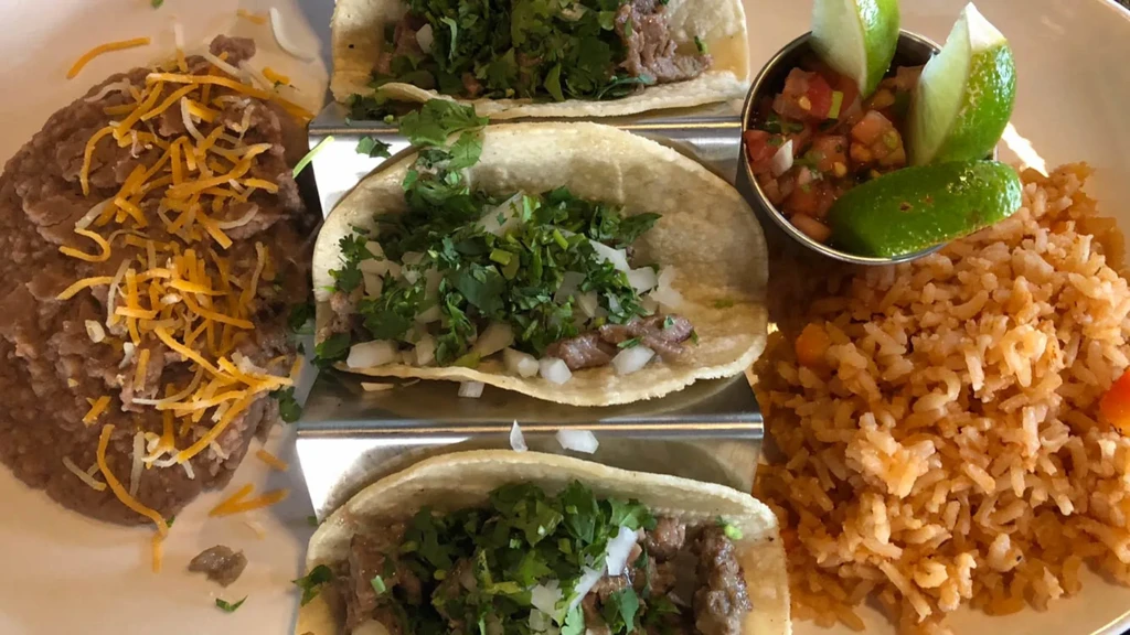 Three street tacos, refried beans, Spanish rice, pico de gallo, and lime.