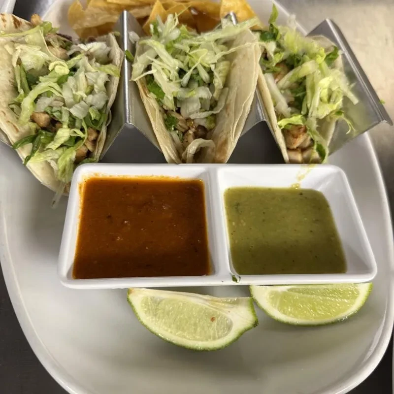 Three tacos with meat, lettuce, two salsas, lime, and chips.