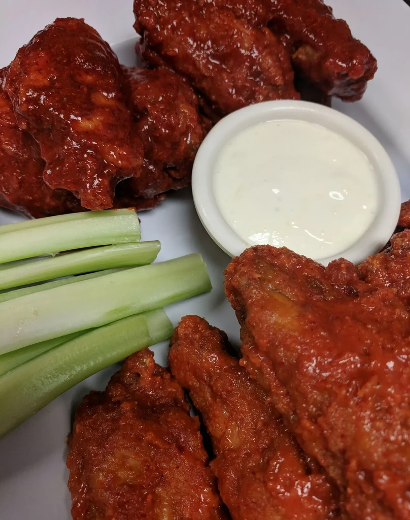 Hot wings, red sauce, creamy dip, and celery on white plate.