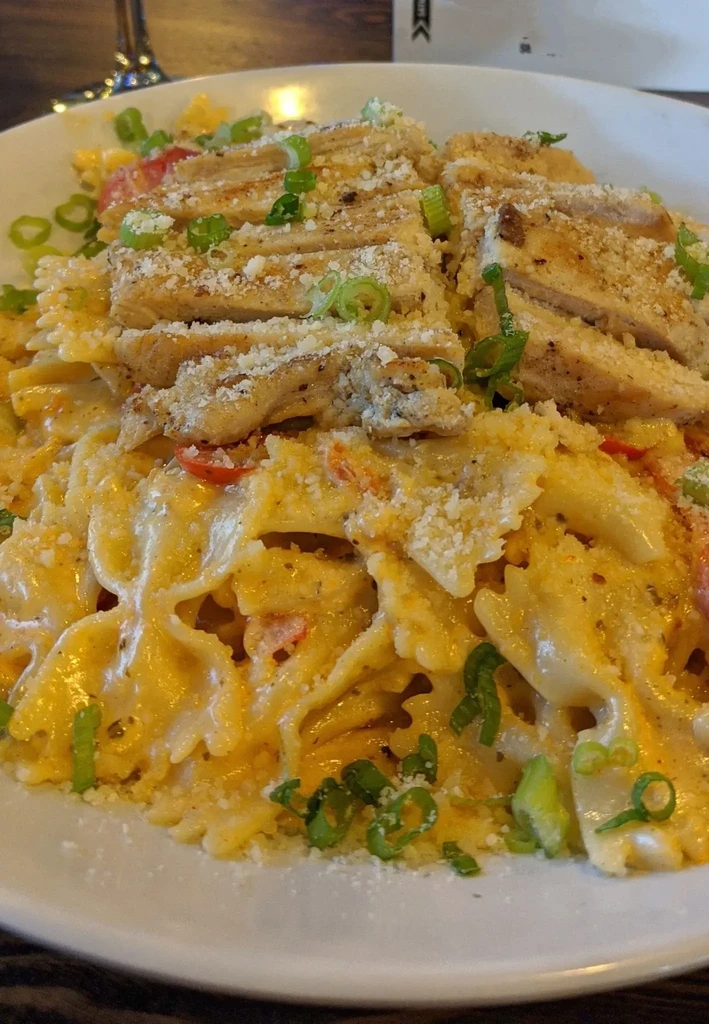 Close-up of creamy farfalle pasta with sliced chicken, cheese, and green onions.