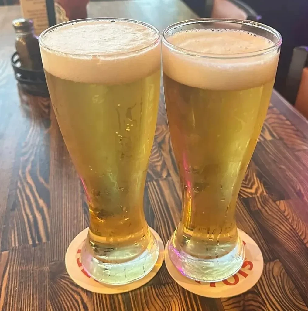Two cold pilsner glasses of golden beer with foam on a wooden table.