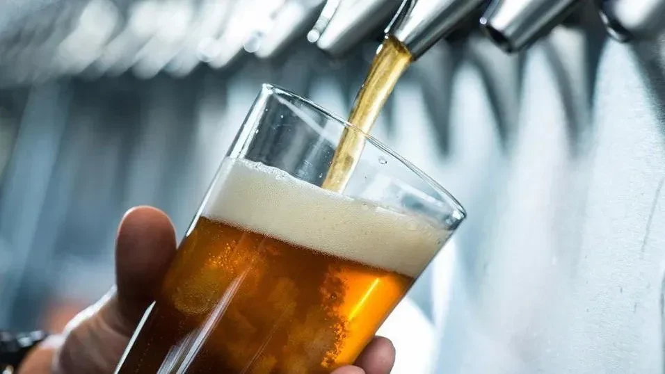 Amber beer pours into a tilted glass from a bar tap.