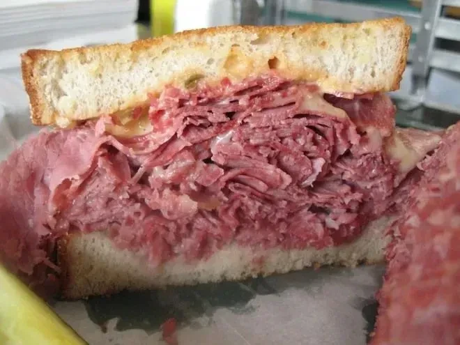 A hearty, cut-in-half pastrami and cheese sandwich with a pickle.