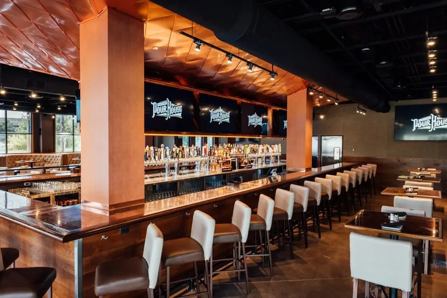Modern "Pour House" bar interior with long counter, taps, and copper ceiling.