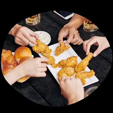 Hands picking up fried chicken and bread from a dark table.