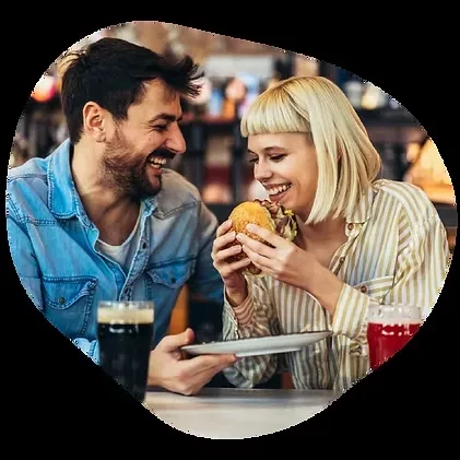Smiling woman about to bite burger, man laughs beside her.