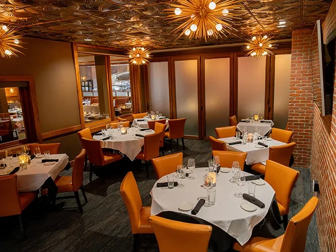 Upscale restaurant dining room with orange chairs and Sputnik chandeliers.