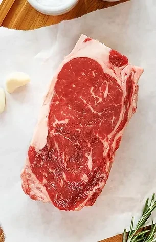 Raw marbled ribeye, garlic, and rosemary on white parchment.