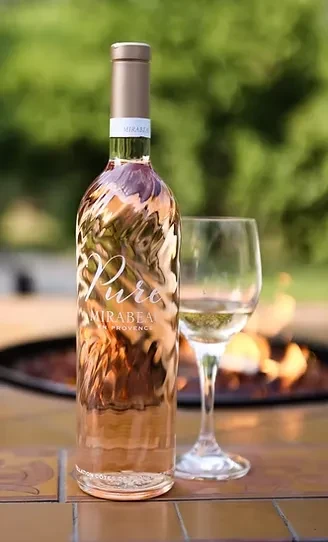 Wavy rosé wine bottle, glass, and fire pit on tile.