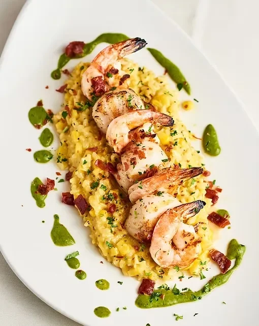 Creamy risotto with five grilled shrimp, herbs, bacon, and green sauce.