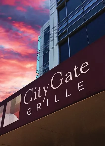 Modern building with "City Gate GRILLE" sign under vibrant sunset sky.