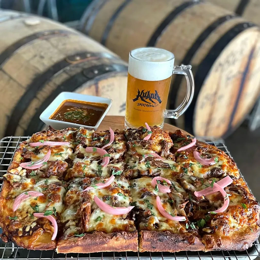 Rectangular pizza with pickled onions, sauce, Kuamu Brewing beer, barrels.