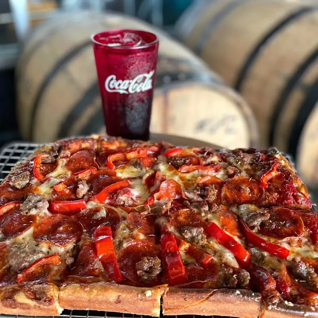 Rectangular deep-dish pizza with pepperoni, sausage, bell peppers, and Coca-Cola.