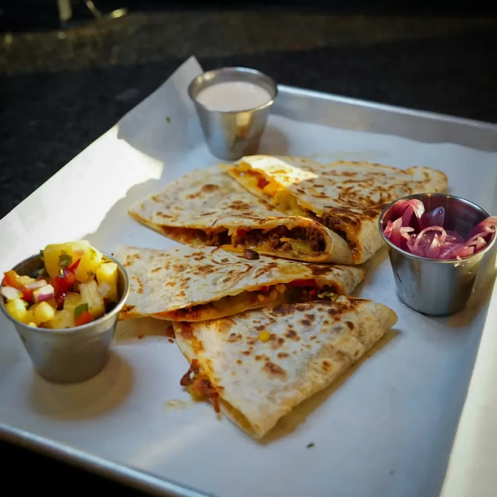 Meat and cheese quesadillas with pineapple salsa, creamy sauce, and pickled onions.